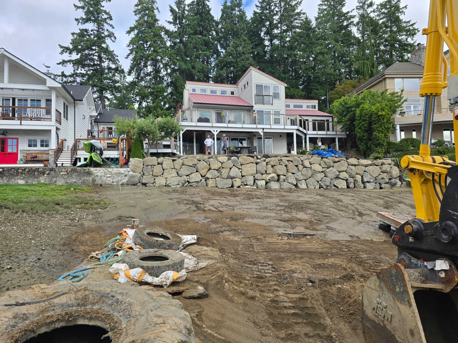 Residential shoreline construction with large rock retaining wall and excavator equipment in the Puget Sound region