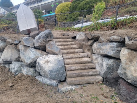 Stone steps built into a boulder retaining wall, part of a landscaped elevation solution near a residential property in the Salish Sea region